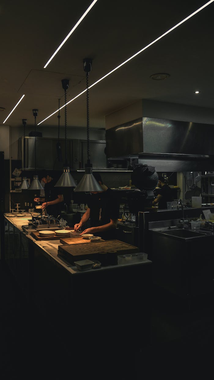 Chefs are carefully preparing food in a dimly lit professional kitchen, showcasing a collaborative cooking environment.