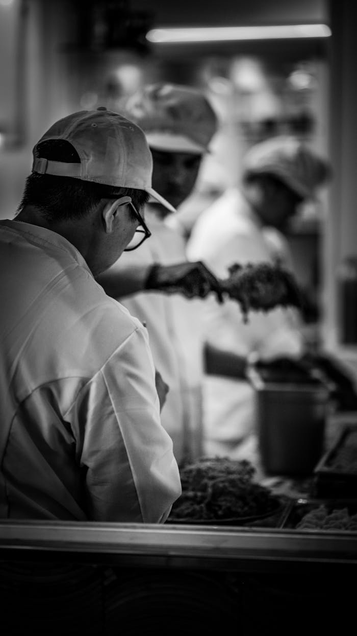 Black and white image of chefs in a kitchen focusing on food preparation in a bustling environment.