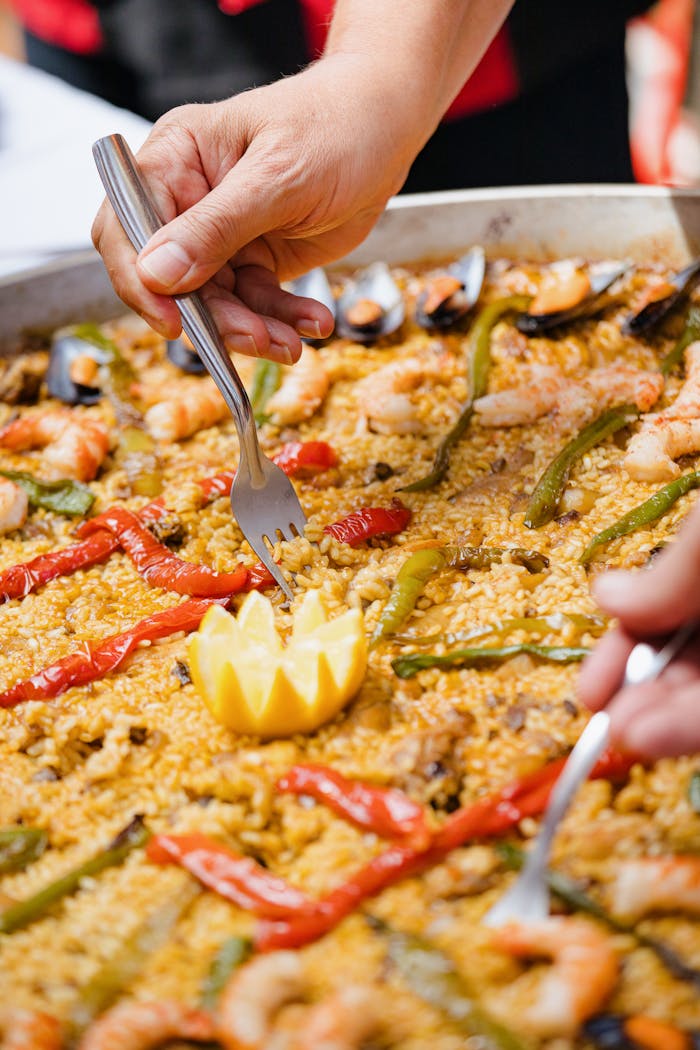 Close-up of hands serving seafood paella with fork, featuring shrimp and vegetables.