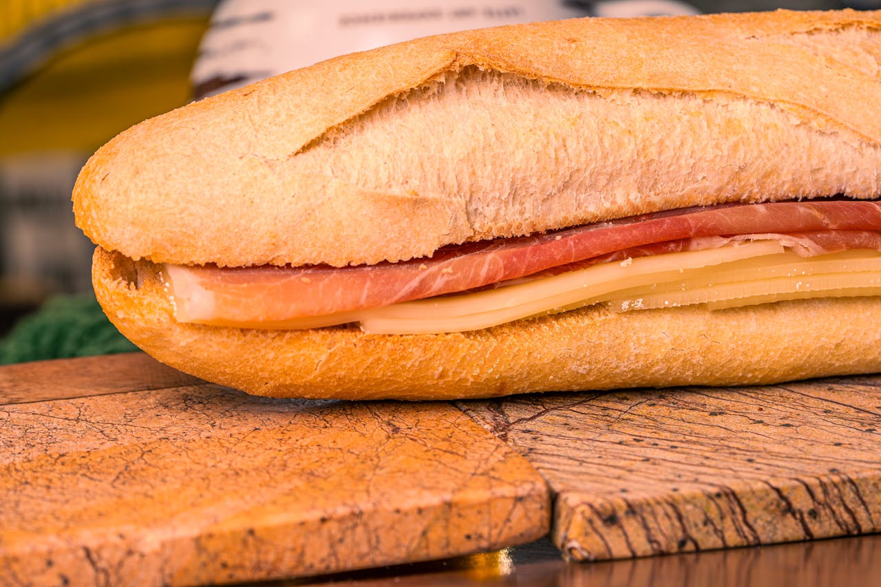 Mouthwatering baguette sandwich with ham and cheese on wooden board.