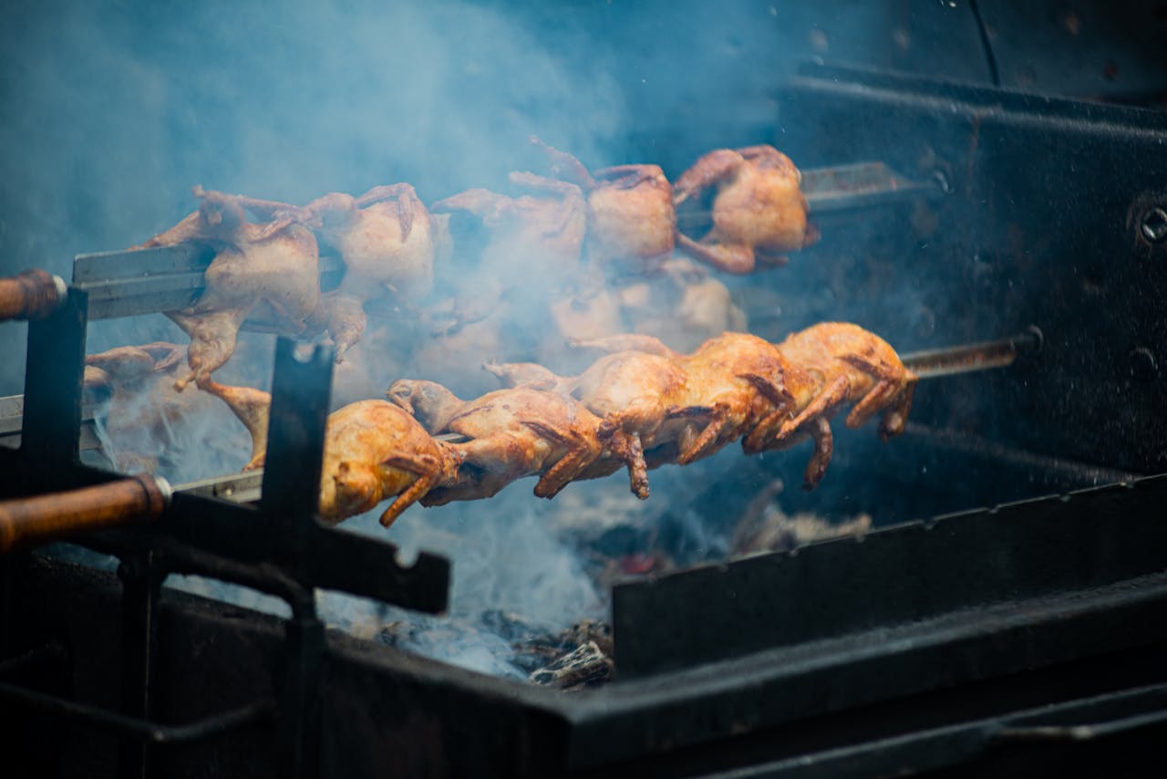 Juicy whole chickens roasting on a spit over open flames outdoors, creating smoky flavors.