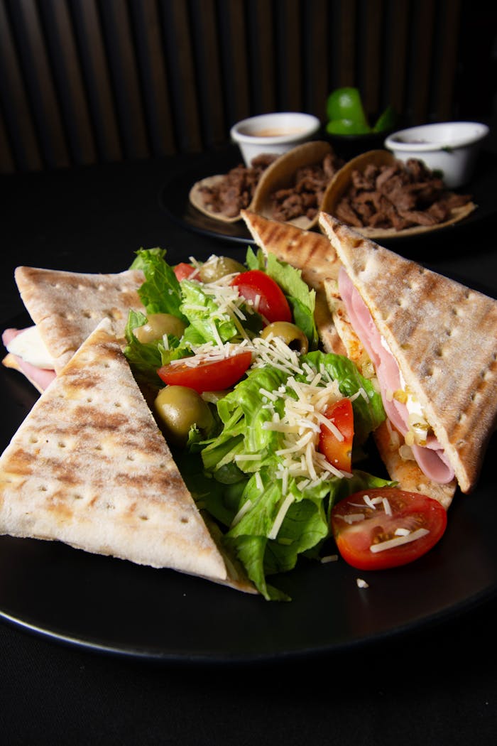 Tasty ham panini with fresh vegetable salad on a black plate, perfect for lunch.